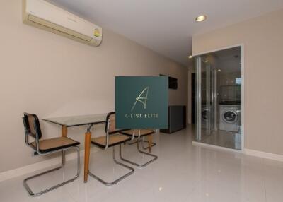 Modern dining area with glass table and washer/dryer in the background