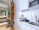 Modern kitchen with white cabinets and appliances, view of the laundry area and bathroom