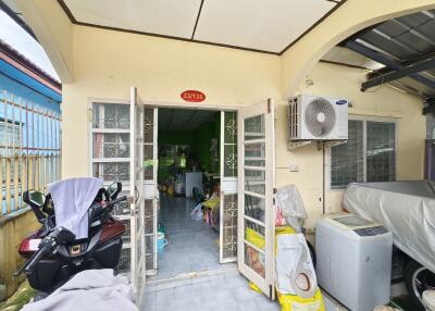 A small building entrance with a view into an interior room, displaying a cluttered area with various items and an air conditioning unit.