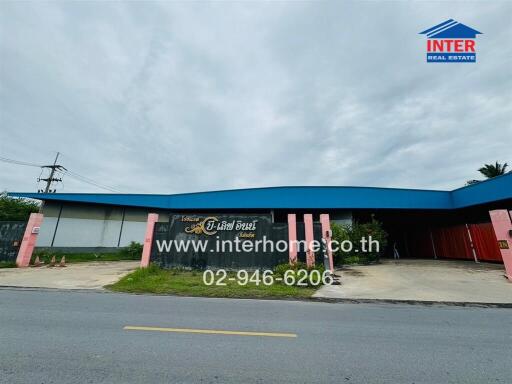 Exterior view of a building with a blue roof and a sign in Thai, including contact information