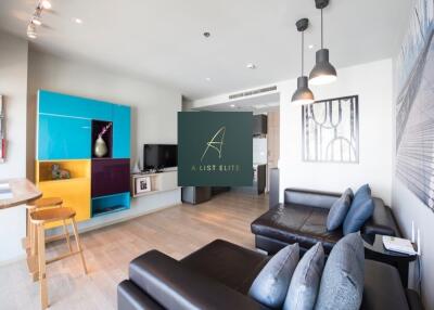 Modern living room with dark sectional sofa, colorful shelving, and pendant lights