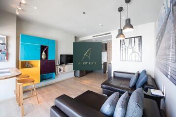 Modern living room with dark sectional sofa, colorful shelving, and pendant lights