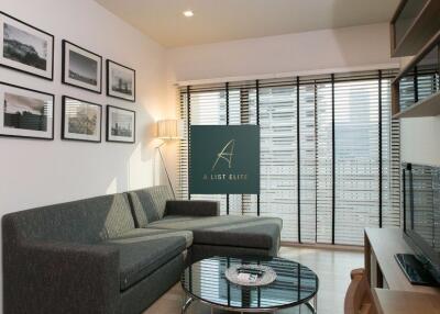 Modern living room with couch, coffee table, framed pictures, and large windows with blinds