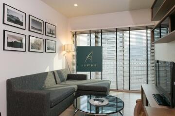 Modern living room with couch, coffee table, framed pictures, and large windows with blinds