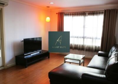 Spacious living room with black leather sofa, TV, and large window