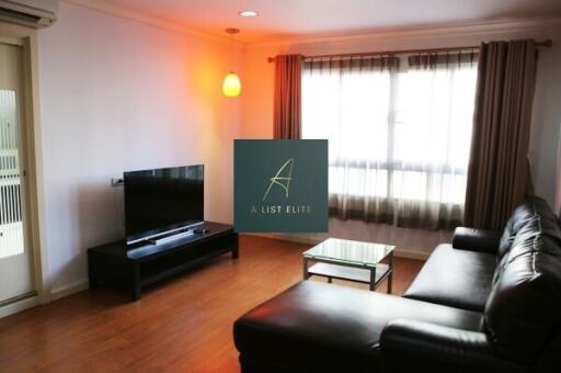 Spacious living room with black leather sofa, TV, and large window