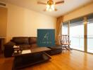 Spacious living room with wood flooring, leather sofa, coffee table, ceiling fan, and large sliding glass doors leading to a balcony.