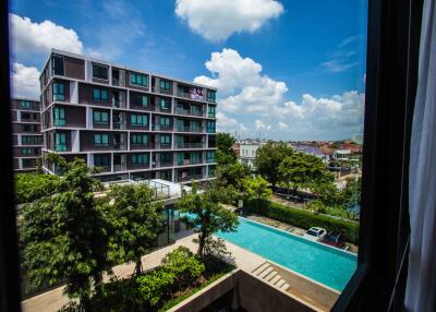 View of apartment complex from a window with swimming pool and lush greenery