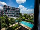 View of apartment complex from a window with swimming pool and lush greenery