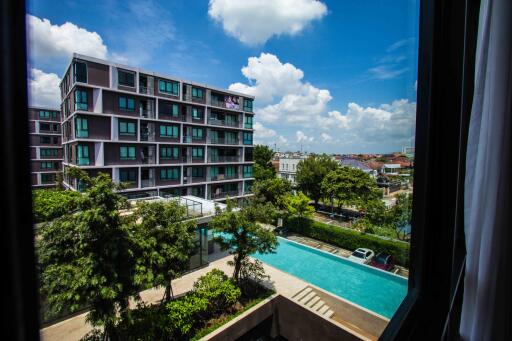 View of apartment complex from a window with swimming pool and lush greenery