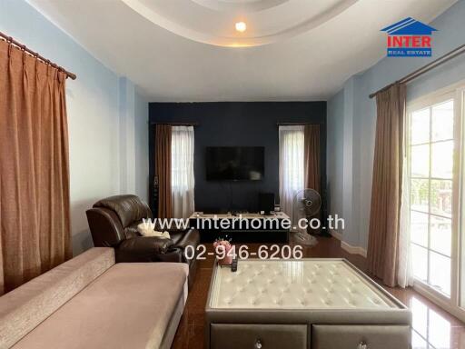 Well-lit living room with a sectional sofa, TV on the wall, and a coffee table with a tufted top