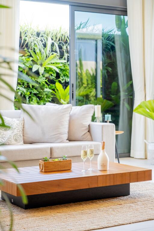 Modern living room with large glass doors, neutral sofa, wooden coffee table, and greenery outside