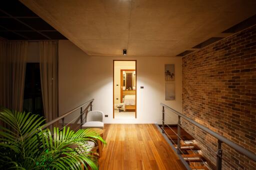 Hallway with wooden flooring and brick accent wall, featuring a view into a lit bedroom