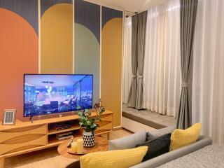 Cozy living room with wall-mounted TV, modern art paneling, large curtains, and a built-in window seat.