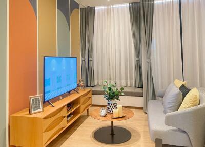 Modern cozy living room with a large window, light wood furniture, and an upholstered grey sofa.