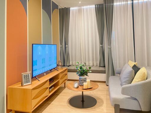 Modern cozy living room with a large window, light wood furniture, and an upholstered grey sofa.