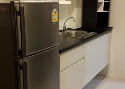 Compact kitchen with refrigerator, microwave, sink, cabinets, and shelves