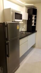 Compact kitchen with refrigerator, microwave, sink, cabinets, and shelves