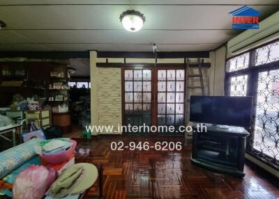 A spacious living room with a TV, wooden floor, and large windows.