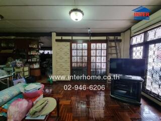 A spacious living room with a TV, wooden floor, and large windows.