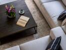 Top view of a modern living room with a coffee table, flowers, and an open book.