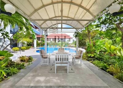 Covered outdoor seating area with building and pool in the background