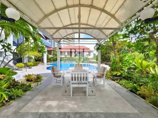 Covered outdoor seating area with building and pool in the background