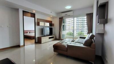 Modern living room with a large couch, wall-mounted TV, and a view into the adjacent bedroom