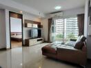 Modern living room with a large couch, wall-mounted TV, and a view into the adjacent bedroom