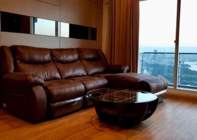 Living room with brown leather sectional sofa, glass-top coffee table, and a large window with a view.