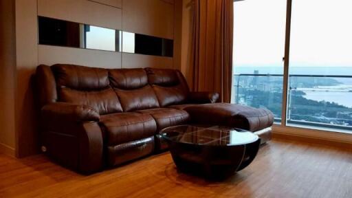 Living room with brown leather sectional sofa, glass-top coffee table, and a large window with a view.