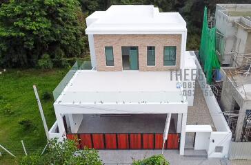 Modern two-story house with a large flat roof, red and white exterior, and a balcony.