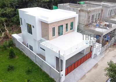 Aerial view of modern two-story house with white exterior and adjacent unfinished building