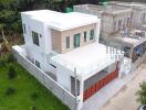 Aerial view of modern two-story house with white exterior and adjacent unfinished building