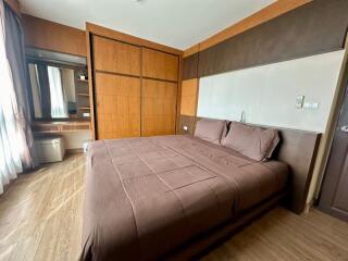 A well-lit bedroom with a large bed, wooden furnishings, and a dressing area.