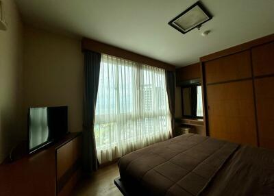 Well-lit bedroom with large window, bed, wardrobe, TV and curtains