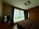 Well-lit bedroom with large window, bed, wardrobe, TV and curtains