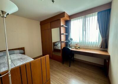 A well-lit bedroom with wooden furniture and a study desk by a window.