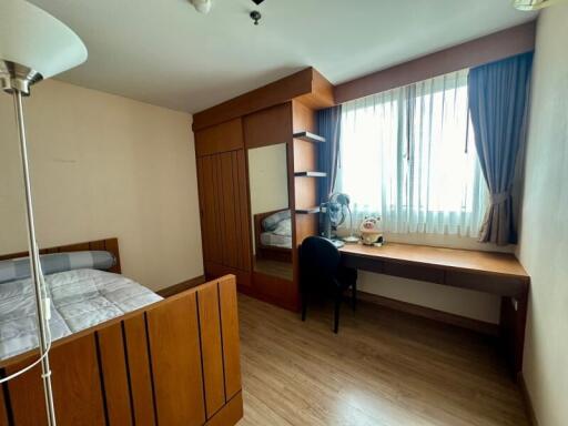 A well-lit bedroom with wooden furniture and a study desk by a window.