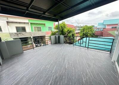 Spacious balcony area with tiled flooring and metal railing, view of neighboring houses and green tree