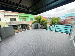 Spacious balcony area with tiled flooring and metal railing, view of neighboring houses and green tree