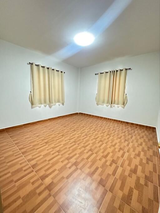 Empty bedroom with tiled floor and two windows with curtains