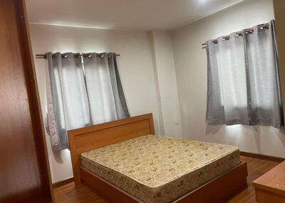 A cozy bedroom with a wooden bed frame and mattress, two windows covered with gray curtains, and a wooden wardrobe.