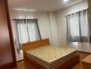 A cozy bedroom with a wooden bed frame and mattress, two windows covered with gray curtains, and a wooden wardrobe.