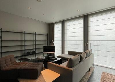 Modern living room with large windows, a couch, recliner, shelves, and a TV