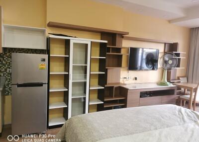 Modern living space featuring a bed, built-in shelving, TV, and dining area