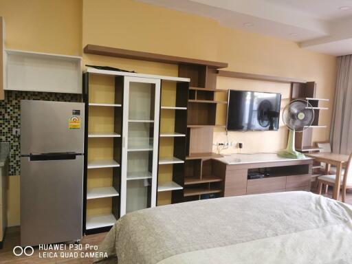 Modern living space featuring a bed, built-in shelving, TV, and dining area