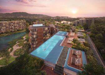 Aerial view of modern residential buildings with a large rooftop pool and lush surroundings at sunset