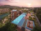 Aerial view of modern residential buildings with a large rooftop pool and lush surroundings at sunset