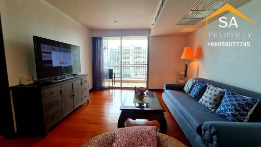 Modern living room with a large TV, comfortable sofa, and a city view balcony